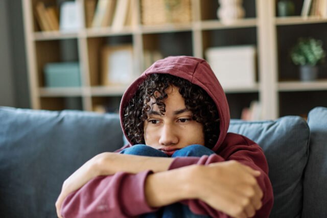 photo - Sad Teenage Boy Sitting Alone on Couch